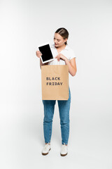 young woman looking at digital tablet with blank screen near shopping bag with black friday lettering on white