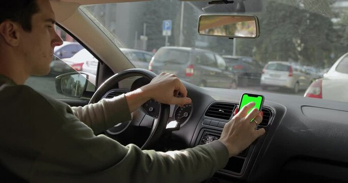 Close-up shot of a man taxi driver staying in the parking lot and using smartphone browsing navigator maps on iPhone connecting or searching for clients. Autumn season. 