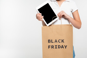 cropped view of woman putting digital tablet with blank screen in shopping bag with black friday lettering isolated on white