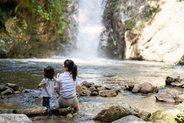Mother and daughter sitting at the rocks against waterfall background.