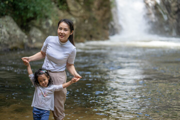 Mother and daughter standing in nature streams against waterfall background.