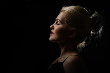 Young beautiful blond glamorous woman in black over dark background