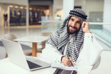 Young Arabian Man Using Phone and Laptop in Cafe.