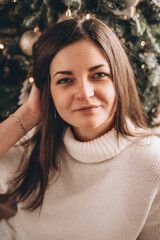 Portrait of a brunette girl in a white sweater near the Christmas tree