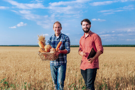 Two guys with a basket of bread staying in the middle of a wheat field