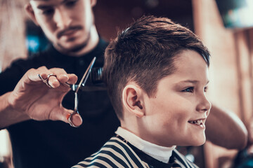 Little boy smile while hairdresser cuts his hair. 