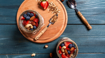 dessert with sweet cream, fresh berries and granola in glass jar on rustic wooden table. healthy breakfast. banner, catering menu recipe place for text, top view
