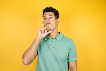 Young handsome man wearing green casual t-shirt over isolated yellow background thinking and looking to the side