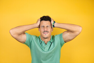 Fototapeta na wymiar Young handsome man wearing green casual t-shirt over isolated yellow background suffering from headache desperate and stressed because pain and migraine with her hands on head
