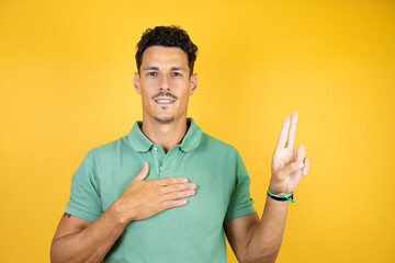 Young handsome man wearing green casual t-shirt over isolated yellow background smiling swearing...