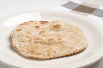 A flatbread on a white plate next to a napkin on the table