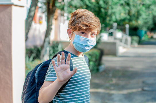 Child Boy In Mask Goes To School And Waving Hand While Greeting. Study During Quarantine Covid-19. Schoolboy Walks. Teen With Backpack. Coronavirus Epidemic