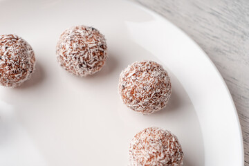 Date candy with coconut shavings on a flat white plate close-up view from above
