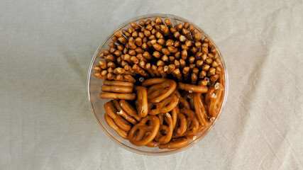 brown straight and twisted salty pretzels in plastic transparent packaging on beige fabric top view