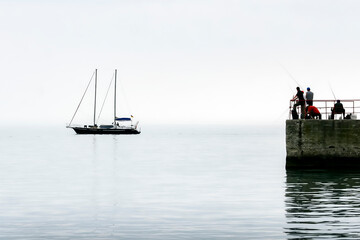 Silhouettes of fishermen on the pier on the background of the silhouette of a yacht on the calm sea.