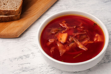 Vegetarian borscht in a white tureen on a light wooden table near pieces of bread