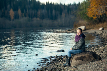 A teenage girl sits on a rock on the Bank of the river.