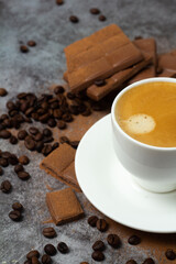 a cup of black strong coffee in a white cup and milk chocolate on a gray background.