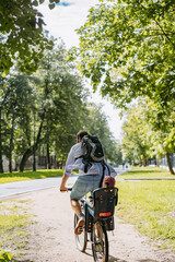 A young man with backpack riding a bike in park  with baby son sitting in child seat