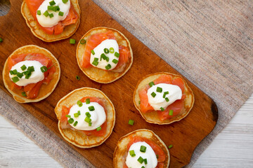 Homemade Blini with Smoked Salmon, Creme and Chives on a rustic wooden board, view from above. Copy space.