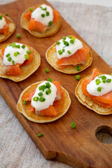 Homemade Blini with Smoked Salmon, Creme and Chives on a rustic wooden board, side view.