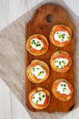 Homemade Blini with Smoked Salmon, Creme and Chives on a rustic wooden board on a white wooden surface, top view. Overhead, from above, flat lay.