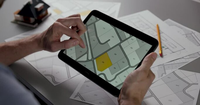 man searching building plot to buy on cadastral plan for house construction on digital tablet