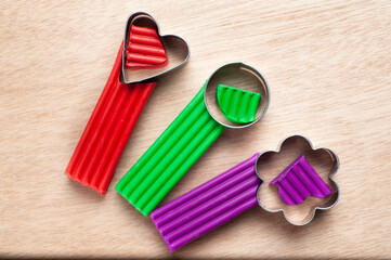 several pieces of plasticine lie on a wooden board with molds in the form of a flower, a heart and a circle