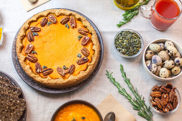 Autumn party, pumpkin dinner: orange soup, pumpkin pie decorated with pecans on a served table and other dishes