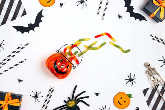 Halloween Holiday Party Background With Gummy Worm, Gifts And Decorations On White Backdrop.