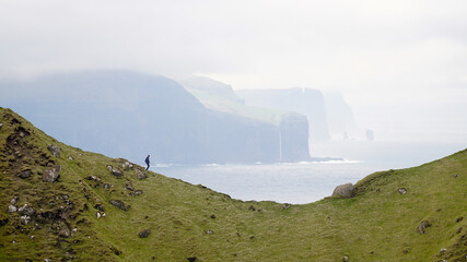 Kallur Lighthouse on Kalsoy Island with green lush cliff landscapes and hikers for perspective in the Faroe Islands, Denmark.