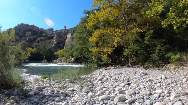 Scenic rock beach by river with woman sunbathing and Italian mountain village in the background.