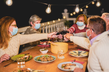 Happy multiracial senior people cheering with red wine at dinner while wearing surgical face mask...
