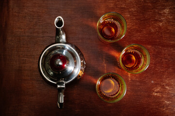 top view of an antique metal teapot with three glass cups on a wooden table