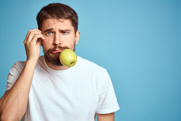 An energetic man with a green apple on a blue background gestures with his hands Copy Space emotions
