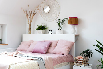 Cozy bedroom with bed, pink pillows and blanket in scandinavian design. Interior of bedroom with white wall, mirror and plants. Comfortable  room in hotel.