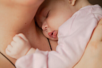 Portrait of a cute newborn baby girl sleeping on her mother's shoulder at home