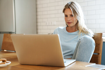 Fototapeta premium Beautiful focused girl using laptop while sitting at table