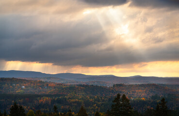 Powerful beams of sunlight breaking through cloudy sky in the afternoon in vermont northeast United States of America during fall shining on a mountain side with vibrant colors of the leaves 