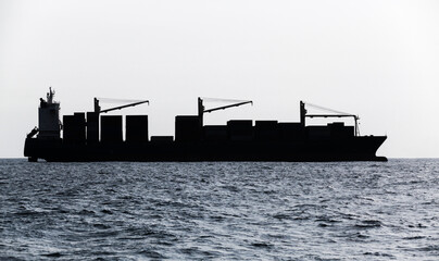 Fototapeta premium Container ship goes on sea. Blue toned silhouette