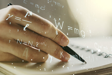 Creative scientific formula hologram with man hand writing in notepad on background, research concept. Multiexposure