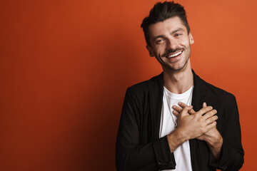 Photo of joyful handsome man smiling and keeping his hands on chest