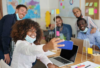 Fototapeta na wymiar Multiracial people in coworking office taking a selfie while wearing surgical face mask under chin - Safety measures in work places