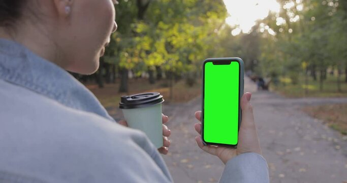 Woman watching on iPhone XS with green screen. Pre keyed and ready for compositing. Coffee and fall background. Online casino, game, conference, video call, youtube, blog. 