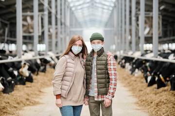 Fototapeta premium Portrait of mother embracing teenage son in mask while they standing in large cowshed