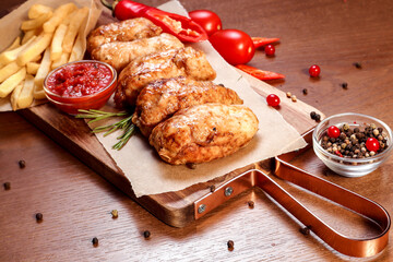 White meat fried chicken on charcoal with sauce and fries on a wooden board.