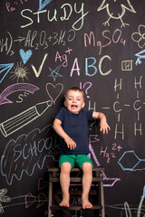 a little three-year-old boy stands near a large slate wall and draws drawings with colored chalk....
