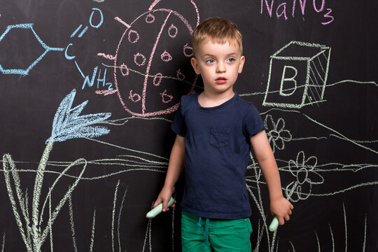 a little Malsik stands near a slate wall and draws with multi-colored chalk. European appearance. learning to draw. look away.