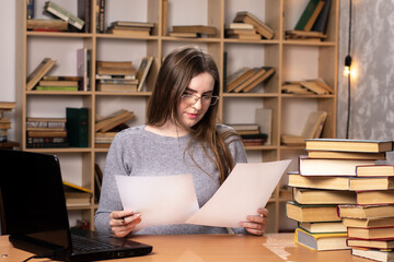 young student prepares for lessons. office worker looks at the documents. a laptop stands on the table and a bookcase in the background. freelancer at work. look at the screen