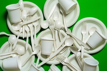 a lot of organic cornstarch forks, spoons, plates and glasses on green background. biodegradable tableware. eco friendly. modern replacement for plastic.